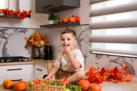 Smiling cute sitting on kitchen table with fruits, autumn leaves and pumpkin Stock Photos