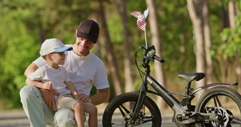 Smiling dad points while son watches pinwheel spinning on bike Vidéo 316760971