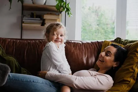Smiling daughter boding with mother lying on sofa in living room Stock Photos