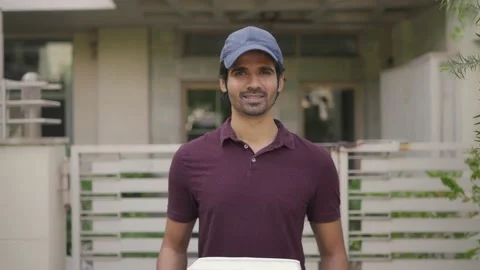A smiling delivery guy holding a box of parcel looking at the camera 스톡 동영상 147340621