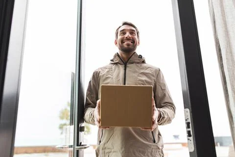 Smiling delivery man with parcel box at open door Stock Photos