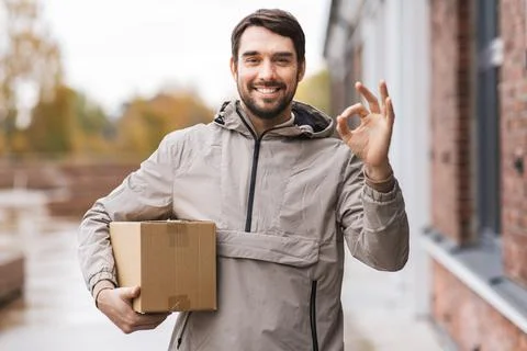 Smiling delivery man with parcel box showing ok Stock Photos