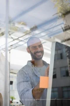 Smiling designer using computer in studio seen through glass Foto stock