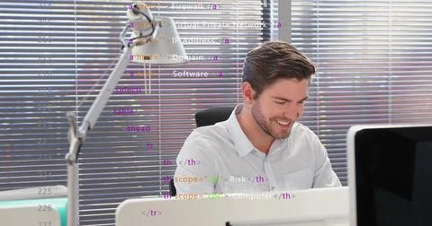 Smiling developer wearing button-down shirt typing code at desk, with dual 写真素材
