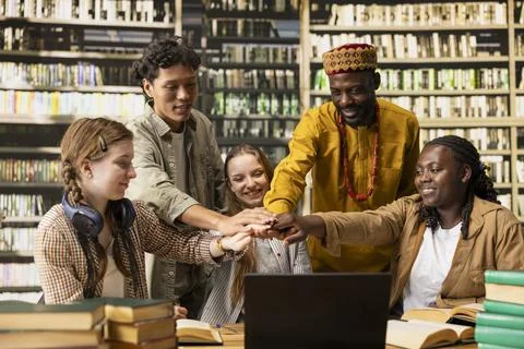 Smiling diverse students stacking hands together in unity at library table Fotos Stock