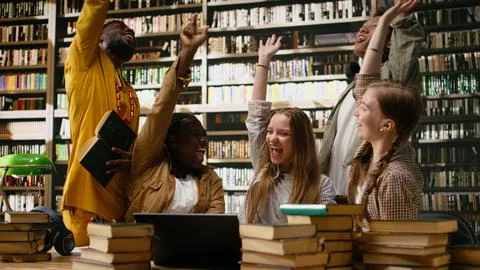 Smiling diverse students stacking hands together in unity at library table Fotos Stock