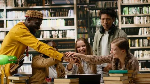 Smiling diverse students stacking hands together in unity at library table Fotos Stock