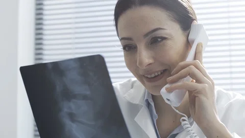 Smiling doctor checking an x-ray and having a phone call Stock Footage 117896615