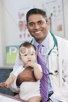 Smiling Doctor Holding Baby In Doctor's Office
