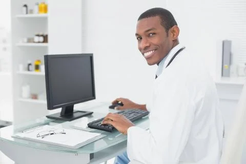 Smiling doctor using computer at medical office 스톡 사진