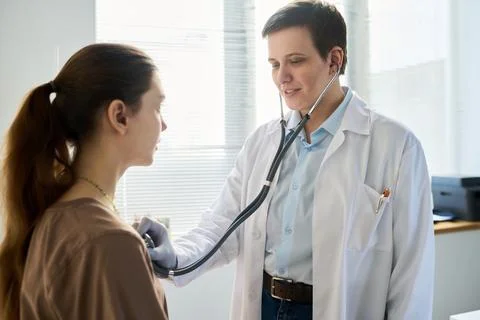 Smiling Doctor Using Stethoscope Checking Patient's Heartbeat 写真素材