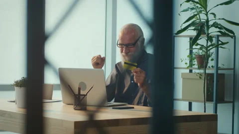 Smiling Elder Man Working Online with Laptop Computer and Using Credit Card Stock Footage 196251325
