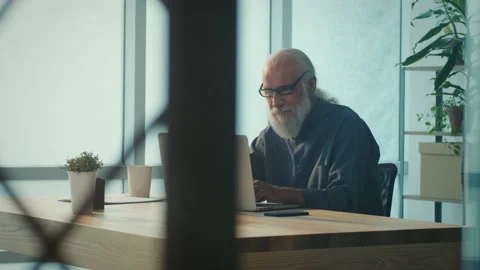 Smiling Elder Man Working Online with Laptop Computer in Bright Room Sitting Video stock 196252452