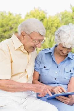 Smiling elderly couple using tablet in the park Foto stock