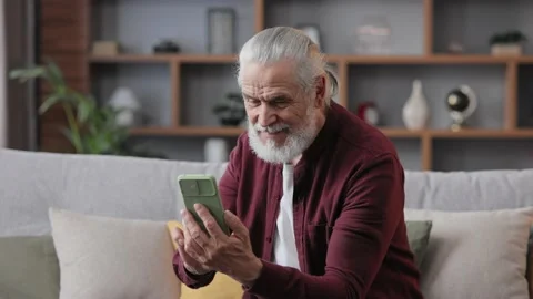 Smiling elderly gray-haired man using smartphone for texting message, playing Stock Footage 197140158