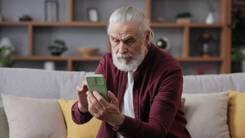 Smiling elderly gray-haired man using smartphone for texting message, playing Stock Footage 200254293