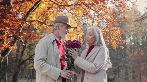 Smiling elderly gray-haired man bringing beautiful bouquet to charming old lady Stock Footage 202180790
