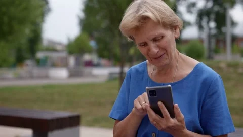Smiling elderly lady using a smartphone to send text messages is sitting on the 動画素材 157448341
