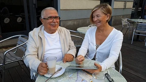 Smiling elderly tourists sit at summer restaurant terrace Stock Footage 127182150