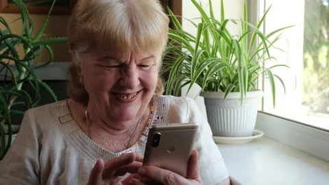 Smiling elderly woman using her phone at home. Grandma is typing text message Video stock 243287805