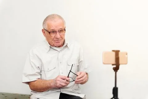 Smiling eldery man looking at camera making video blog or call at home sittin Stock Photos