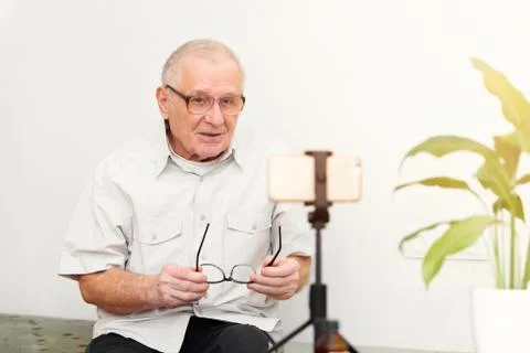 Smiling eldery man looking at camera making video blog or call at home sittin Stock Photos
