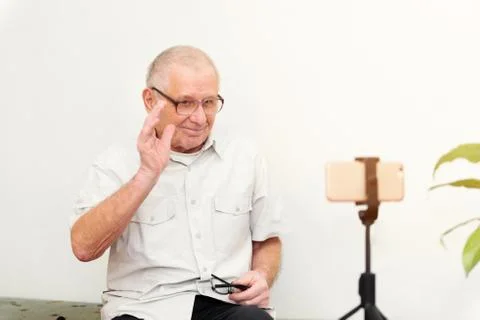 Smiling eldery man looking at camera making video blog or call at home sittin Stock Photos