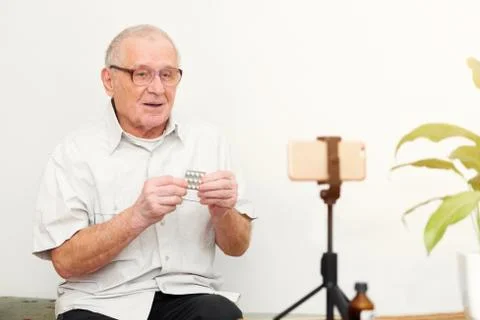 Smiling eldery man looking at camera making video blog or call at home sittin Stock Photos