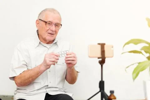 Smiling eldery man looking at camera making video blog or call at home sittin Stock Photos