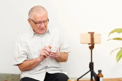 Smiling eldery man looking at camera making video blog or call at home sittin Stock Photos