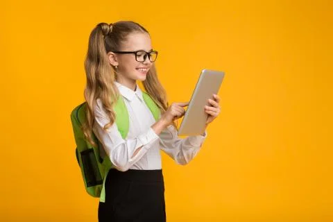 Smiling Elementary School Girl Using Digital Tablet Over Yellow Background Stock Photos