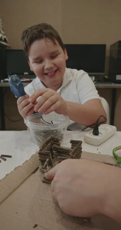 A smiling elementary school student builds a small model house out of cardboard Video stock 327601395