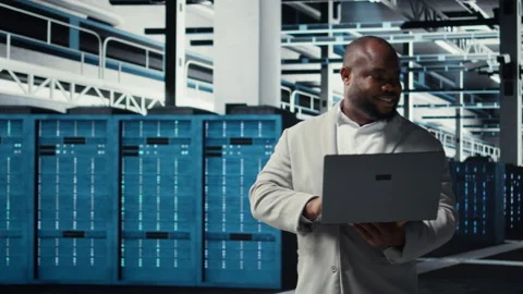 Smiling engineer in data center managing software using laptop Stock Footage 311897448