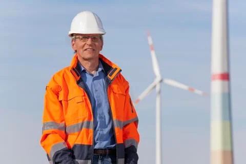Smiling engineer with hard hat and protective clothing in front of windmills 写真素材