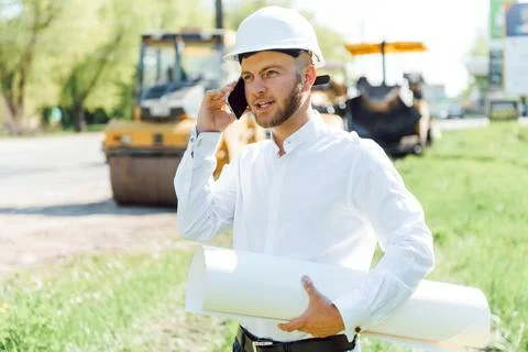 Smiling engineer with helmet standing in front of excavator on road constru.. Stock Photos