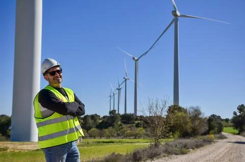 Smiling engineer posing with crossed arms in front of wind turbines farm Stock Photos