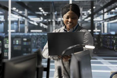 Smiling engineer using laptop in data center to oversee hardware Stock Photos