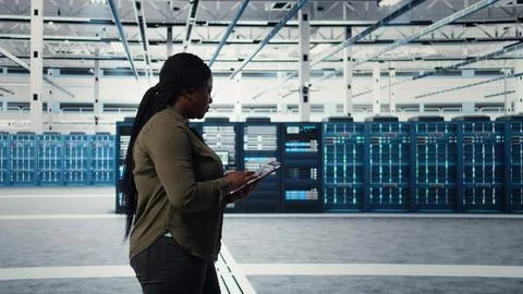 Smiling engineer walking in data center with laptop, checking hardware 库存照片