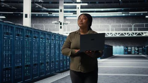 Smiling engineer walking in data center with laptop, checking hardware Stock Photos
