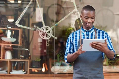 Smiling entrepreneur using a tablet in front of his cafe Stock Photos