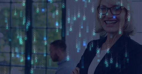 Smiling exec wearing dark blazer, glasses standing at office windows with binary Foto stock
