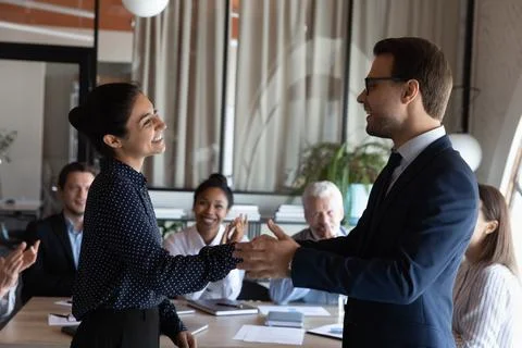 Smiling executive shaking Indian businesswoman hand at corporate meeting Stock Photos