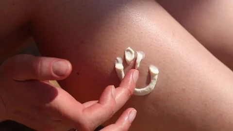 Smiling face design with sunscreen on a woman's leg Stock Footage 313551498