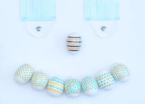 Smiling face made of decorated Easter eggs and medical face masks on white ba Stock Photos