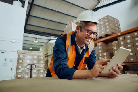 Smiling factory worker leaning on table at warehouse looking at digital tablet Stock Photos