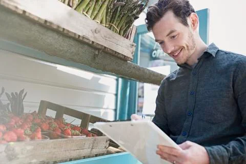 Smiling farmerís market worker checking inventory with clipboard next to Stock Photos