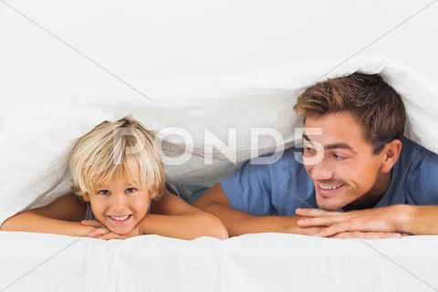Smiling father and his son lying under the duvet Stock Photos