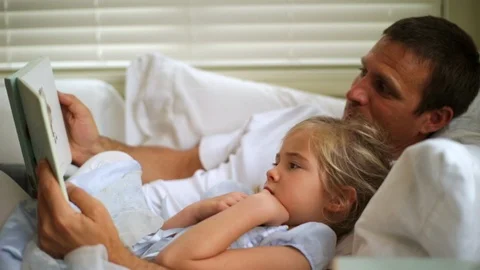 Smiling father and his young daughter enjoy reading a picture book together on 库存影片 88444652