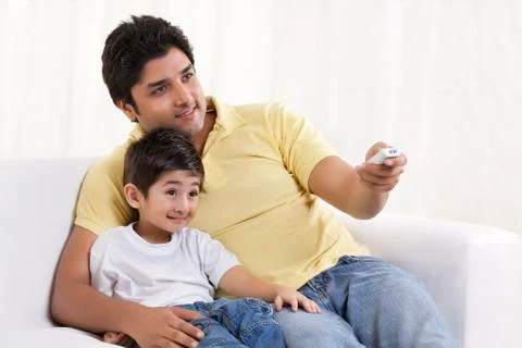 Smiling father changing channels while sitting with his son Stock Photos