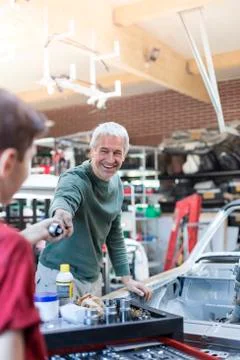 Smiling father taking tool from son in auto repair shop Stock Photos